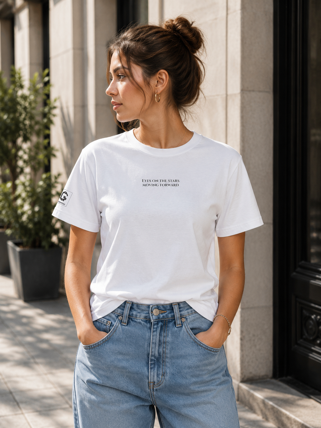 Woman wearing a white t-shirt with a text "Eyes on the stars - moving forward" and blue jeans standing on a street.